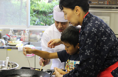 「老舗料亭　助六」の女将と料理人が、子供に和食の作り方を直接教える様子